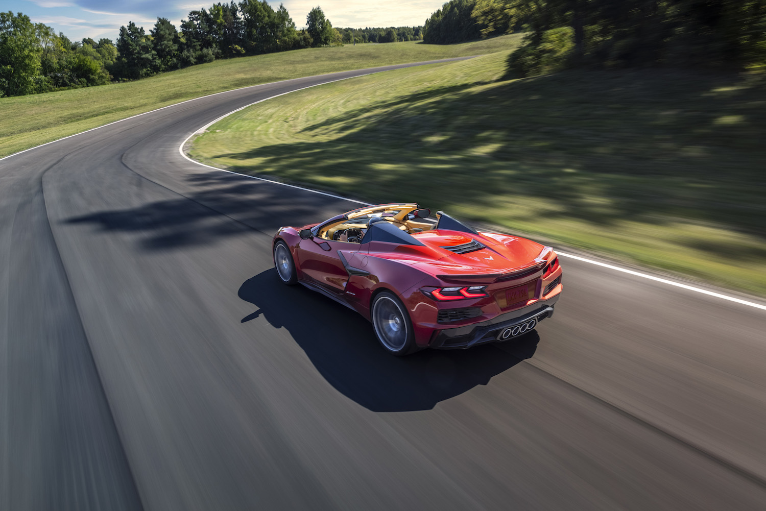 Red Chevrolet Corvette Z06 supercar with its top down driving on a country road.