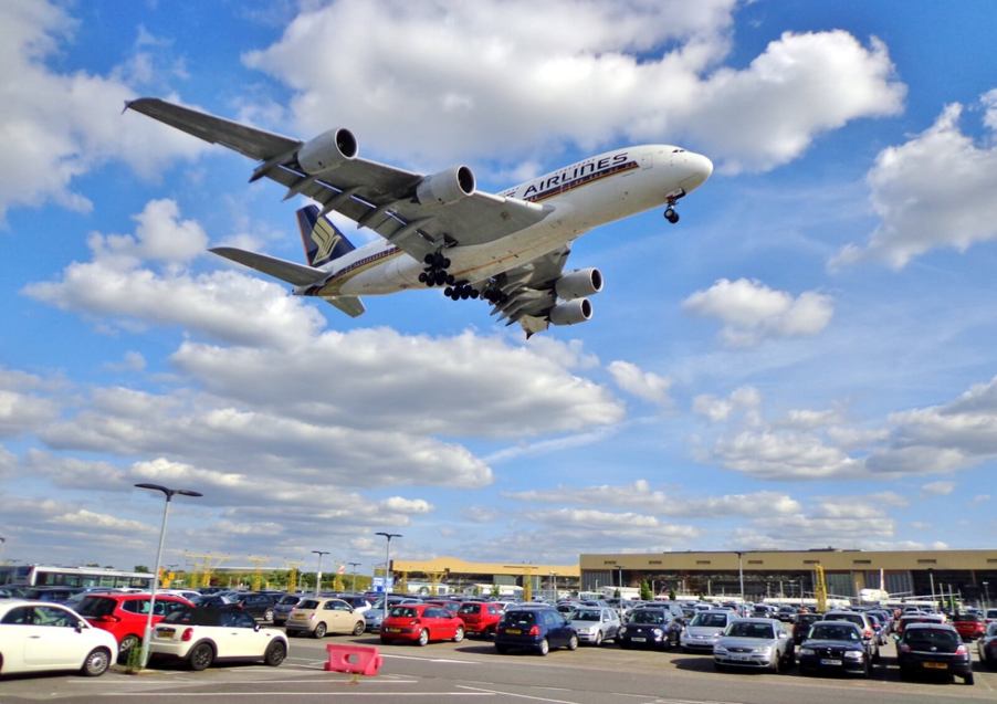 A busy airport parking lot with a commercial airline flying overhead.