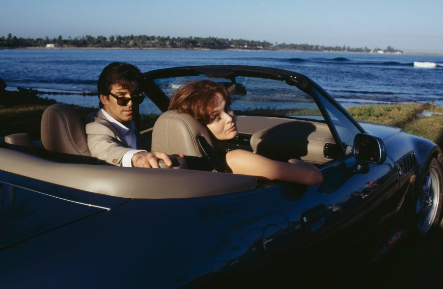 James Bond and his passenger look backward out of a BMW Z3 convertible during the "Goldeneye" film, the ocean visible in the background.
