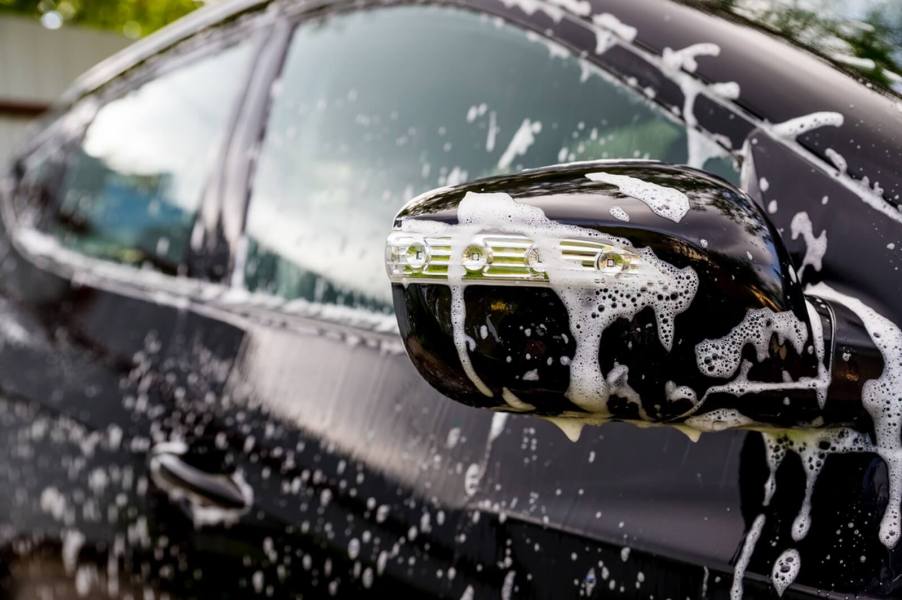A car wash features a black hatchback covered in suds and soap.