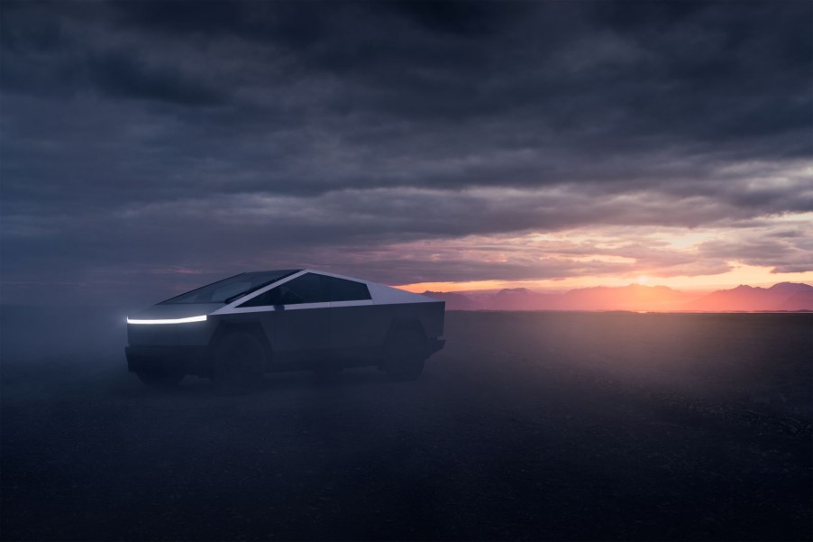 A 2024 Tesla Cybertruck sits on a dirt road with mountains in the background, highlighted by a sunset