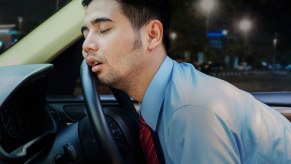 Young man sleeping against the steering wheel of a car.
