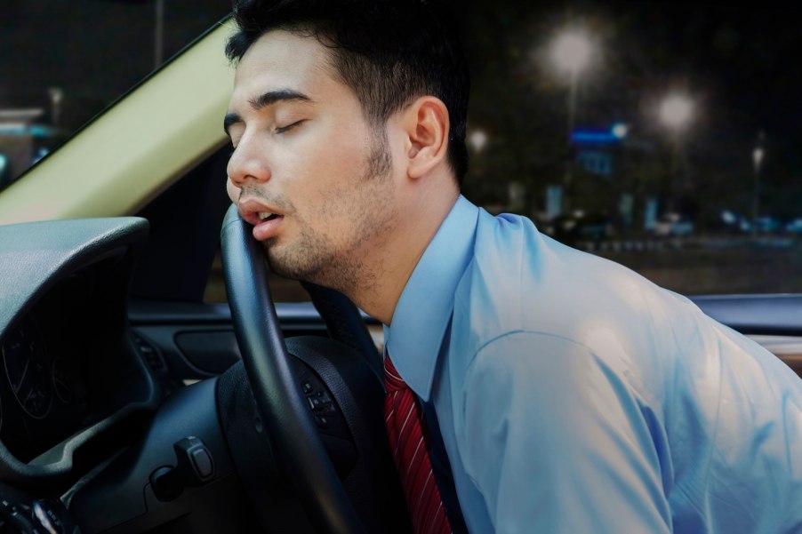 Young man sleeping against the steering wheel of a car.