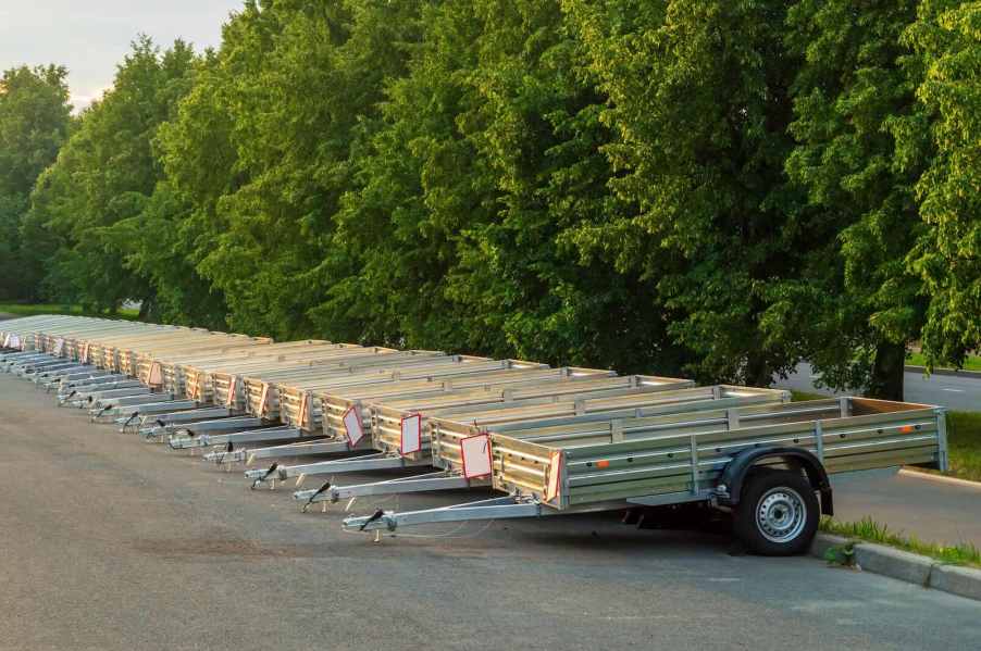 Row of rental trailers in a parking lot, trees visible in the background.