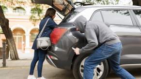 Man in a hood holding a knife stalks a driver who has opened the back of her car.