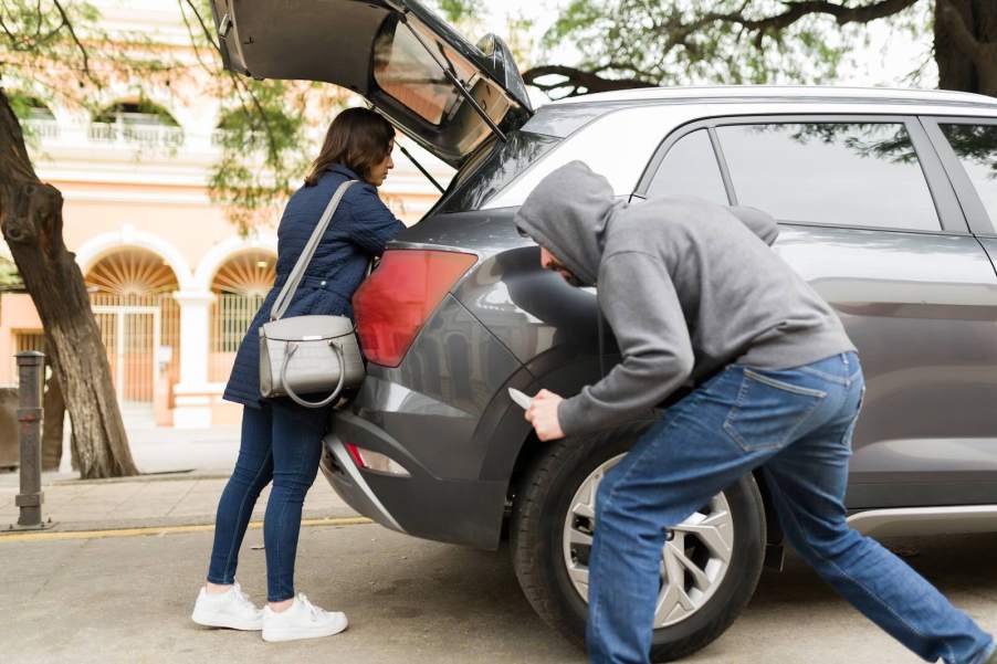 Man in a hood holding a knife stalks a driver who has opened the back of her car.