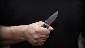 Man's fist clenched around a folding, fighting knife.