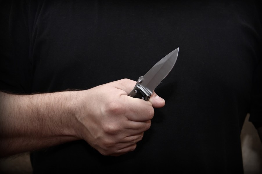 Man's fist clenched around a folding, fighting knife.