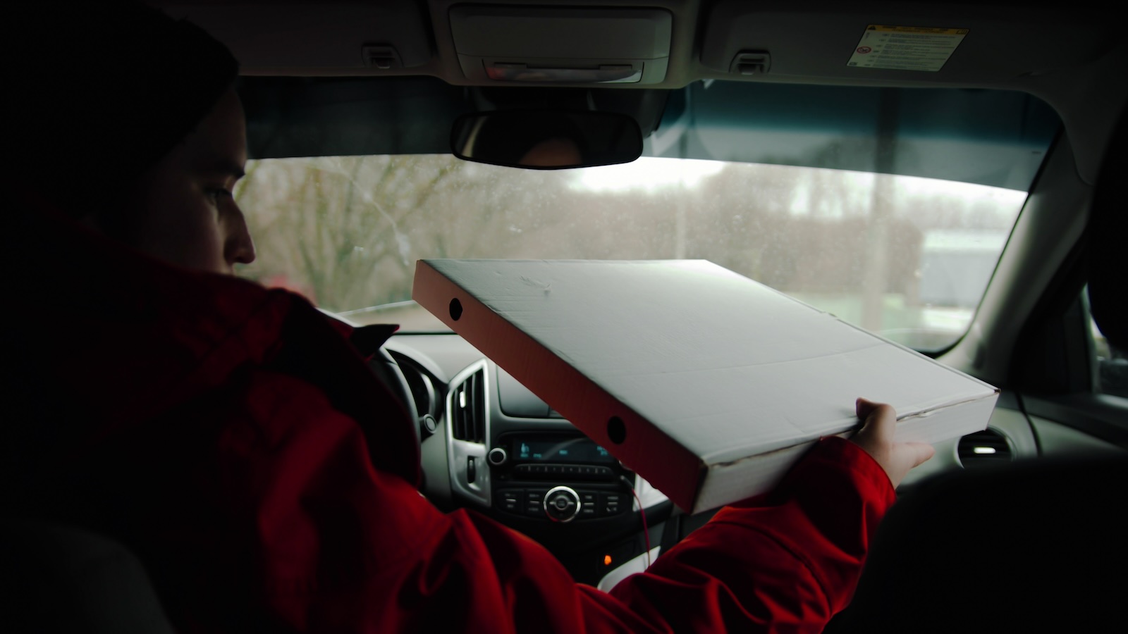 Delivery driver holding a pizza box in his car.