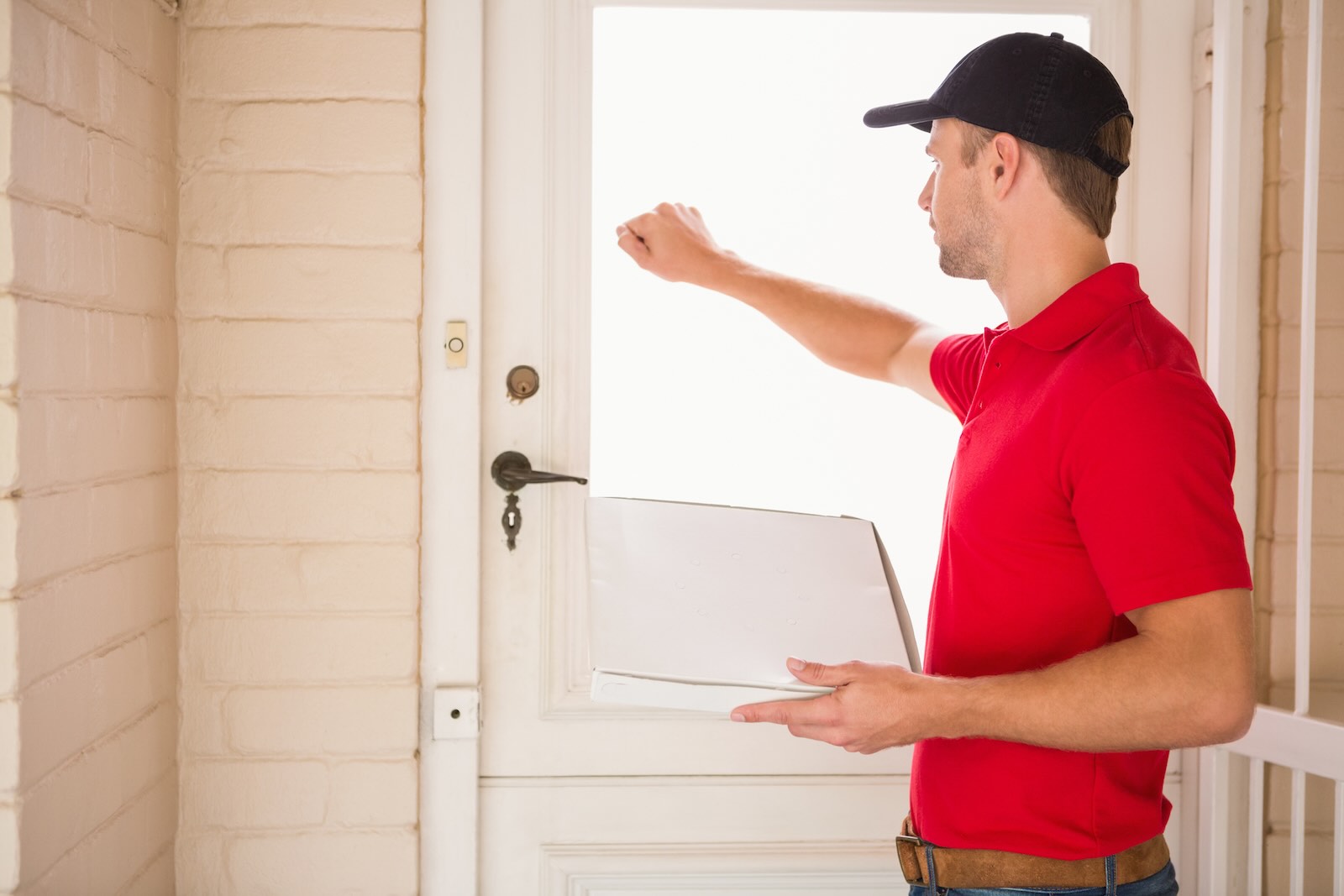 Delivery driver holding a pizza and knocking on a door.