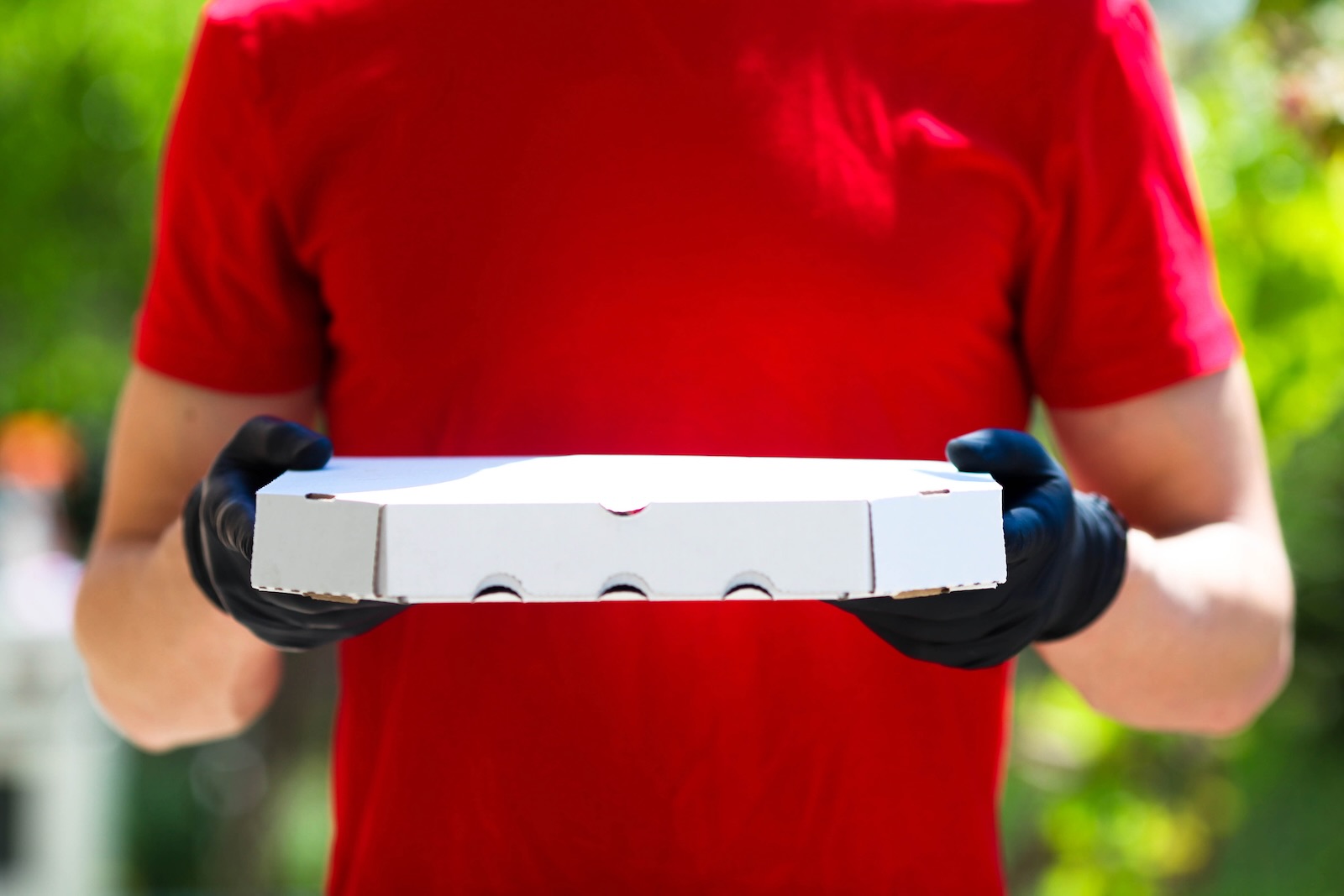 The hands of a pizza delivery driver holding a box.