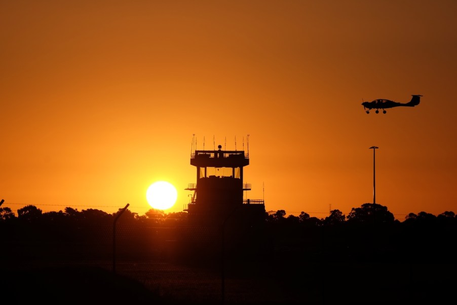 Small airplane passing an airport tower, the setting sun silhouetting the scene.