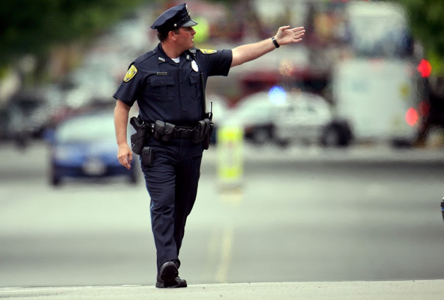 Police officer stands in the middle of the street and holds up his hand to give a command.