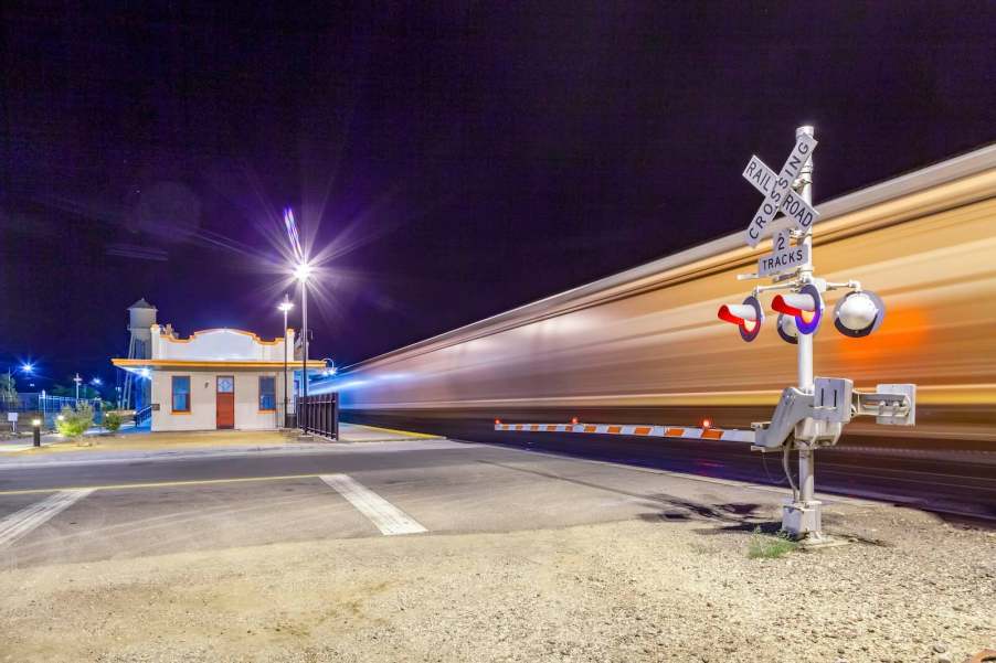 Train whizzes by a railroad crossing in a small town at night.