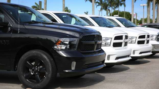 Car lot full of used Ram 1500 pickup trucks from various model years for sale, palm trees visible in the background.