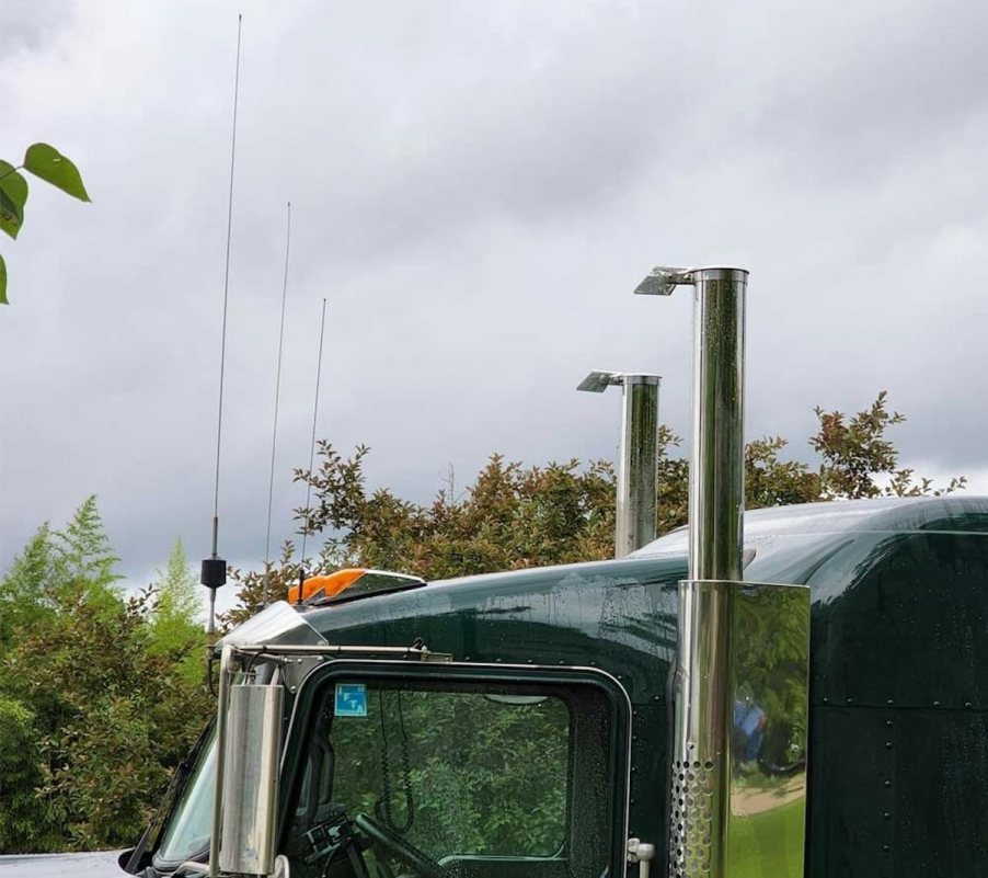 The upward-facing exhaust stacks above a semi truck tractor, trees visible in the background.