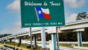 Green welcome sign by a Texas highway that says "Drive Friendly--The Texas Way"