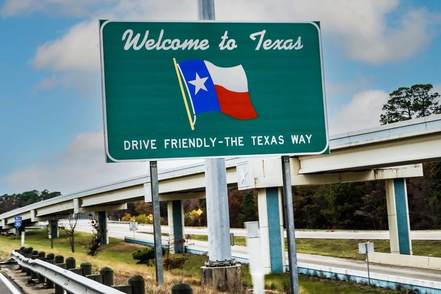 Green welcome sign by a Texas highway that says "Drive Friendly--The Texas Way"