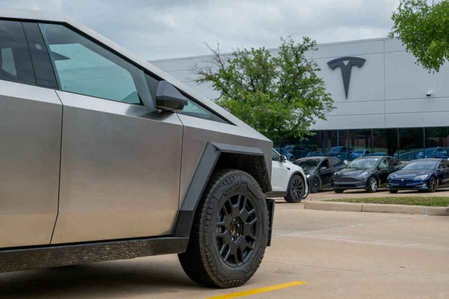 A Tesla Cybertruck parked at a Tesla dealership with different Tesla models in the background