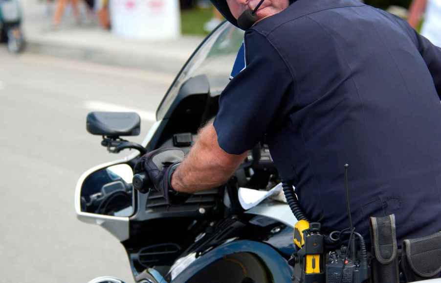 A deputy police officer riding a motorcycle looks over his left shoulder close camera view from behind