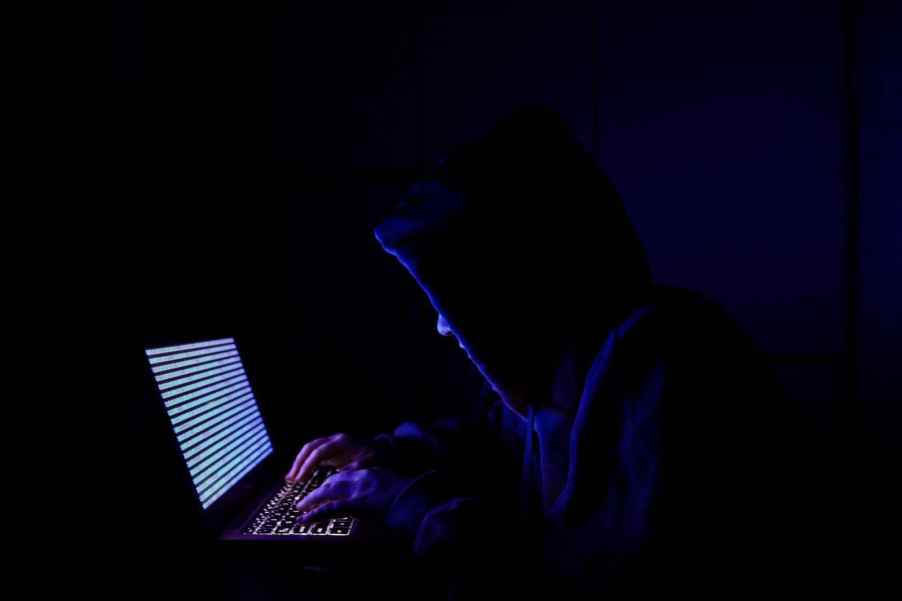 A person sitting at a laptop computer in the dark attempting to hack into a mainframe