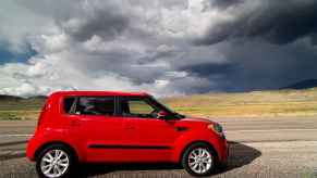 A red Kia Soul parked on the side of the road with storm clouds in the distance