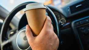 A man's hand holds a coffee cup inside a car