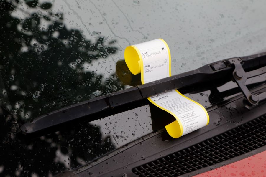 A parking ticket pinned to a car's windshield by a wiper blade