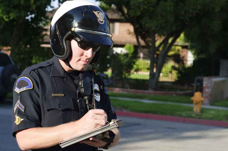 Police officer standing writing a traffic ticket citation wearing a motorcycle helmet