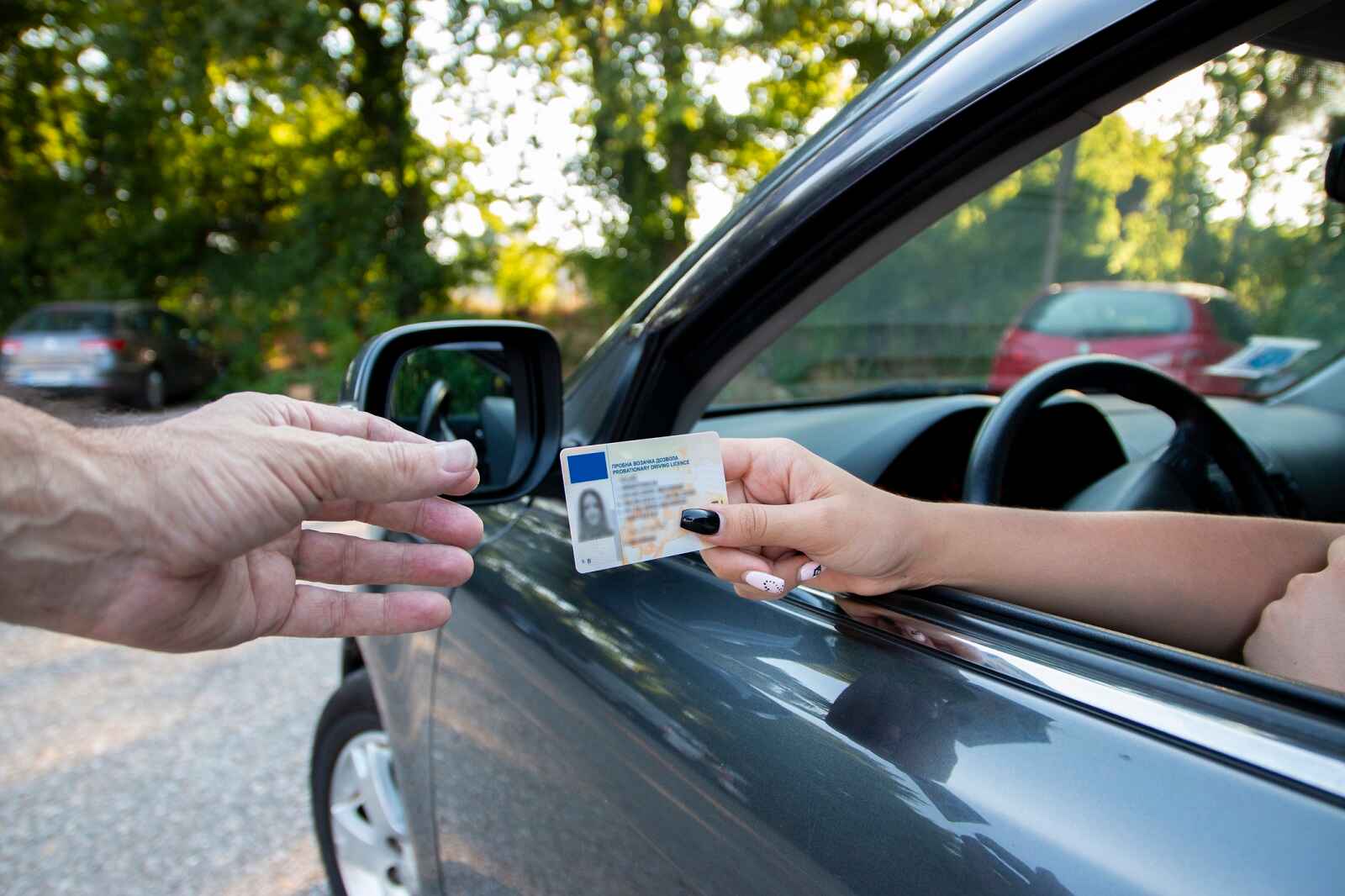 A woman driver's hand giving a driver's license over to a man's hand outside of a car in close view during traffic stop