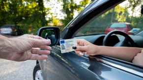A woman driver's hand giving a driver's license over to a man's hand outside of a car in close view during traffic stop
