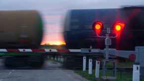 A train crossing past the viewer at dusk with red railroad crossing lights illuminated