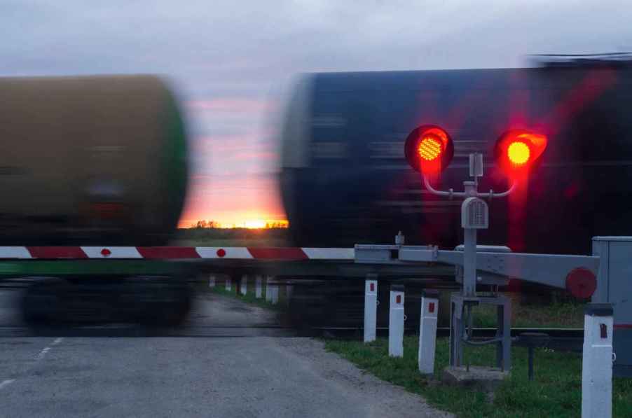 A train crossing past the viewer at dusk with red railroad crossing lights illuminated