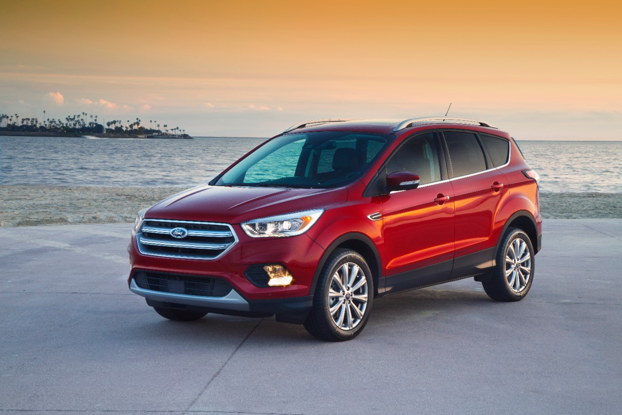 A red 2017 Ford Escape parked in front of a sunset and water in left front angle view