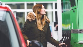 A woman uses a gas station pump to fuel her car.