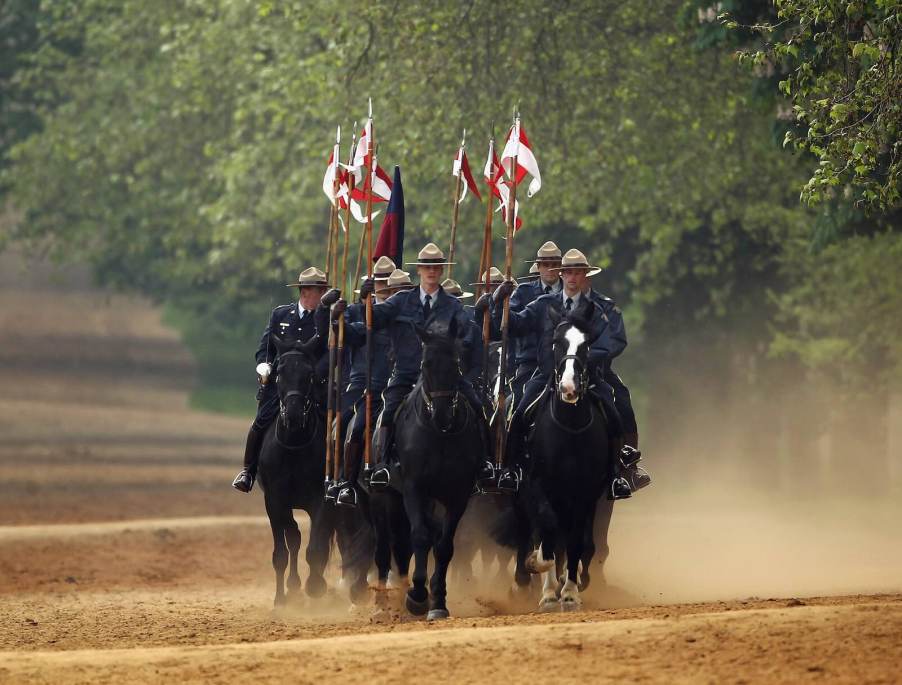 A row of Canadian Mounties police officers riding horses through the woods.