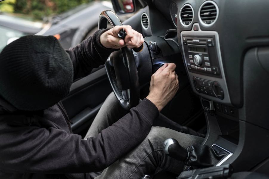 A car thief works on the latest of his stolen cars in a parking lot.
