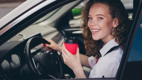 A woman at the wheel of a car holds up a to-go cup of tea