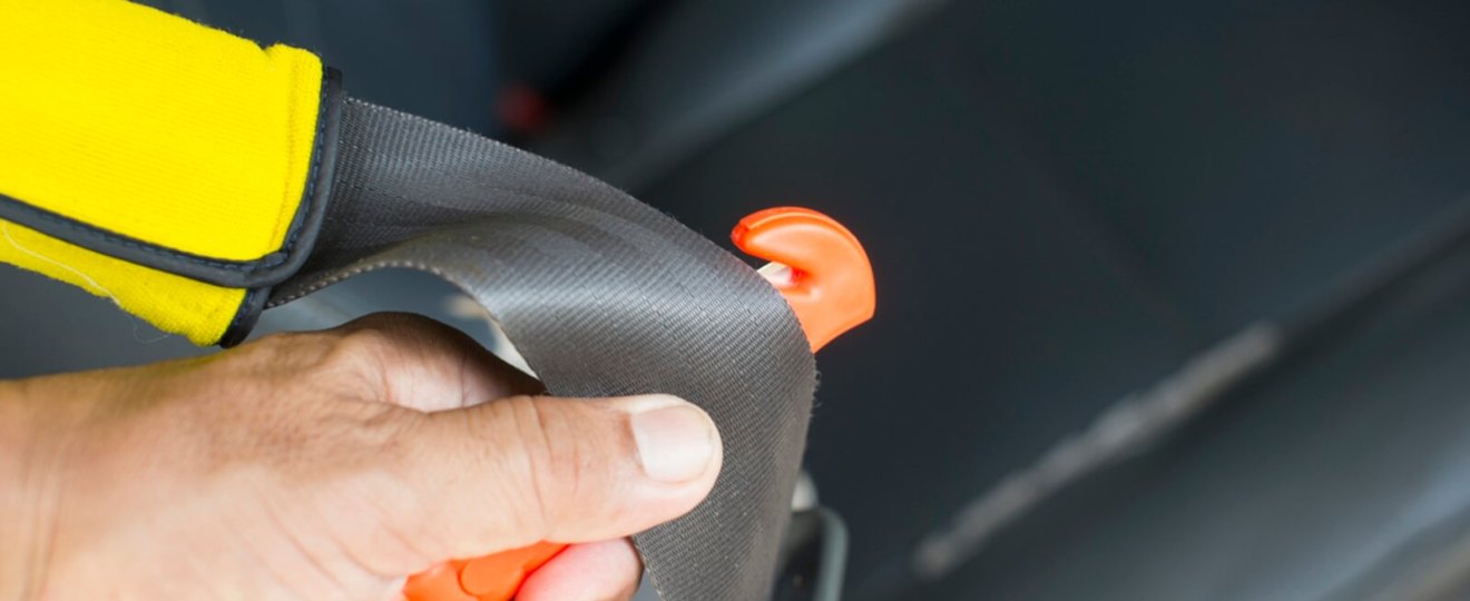 A driver uses a seatbelt cutter to slash a belt.