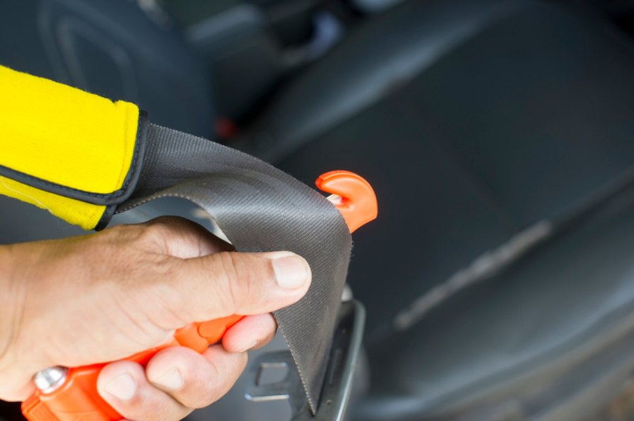 A driver uses a seatbelt cutter to slash a belt.