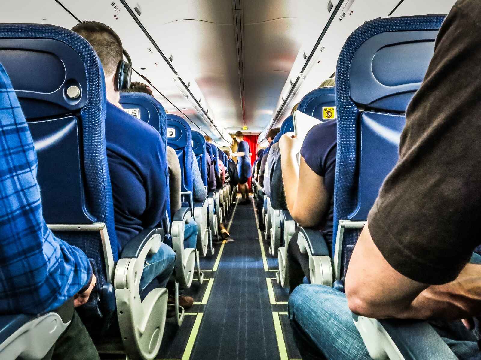 The inside of a commercial plane filled with passengers view from the aisle looking toward the cockpit