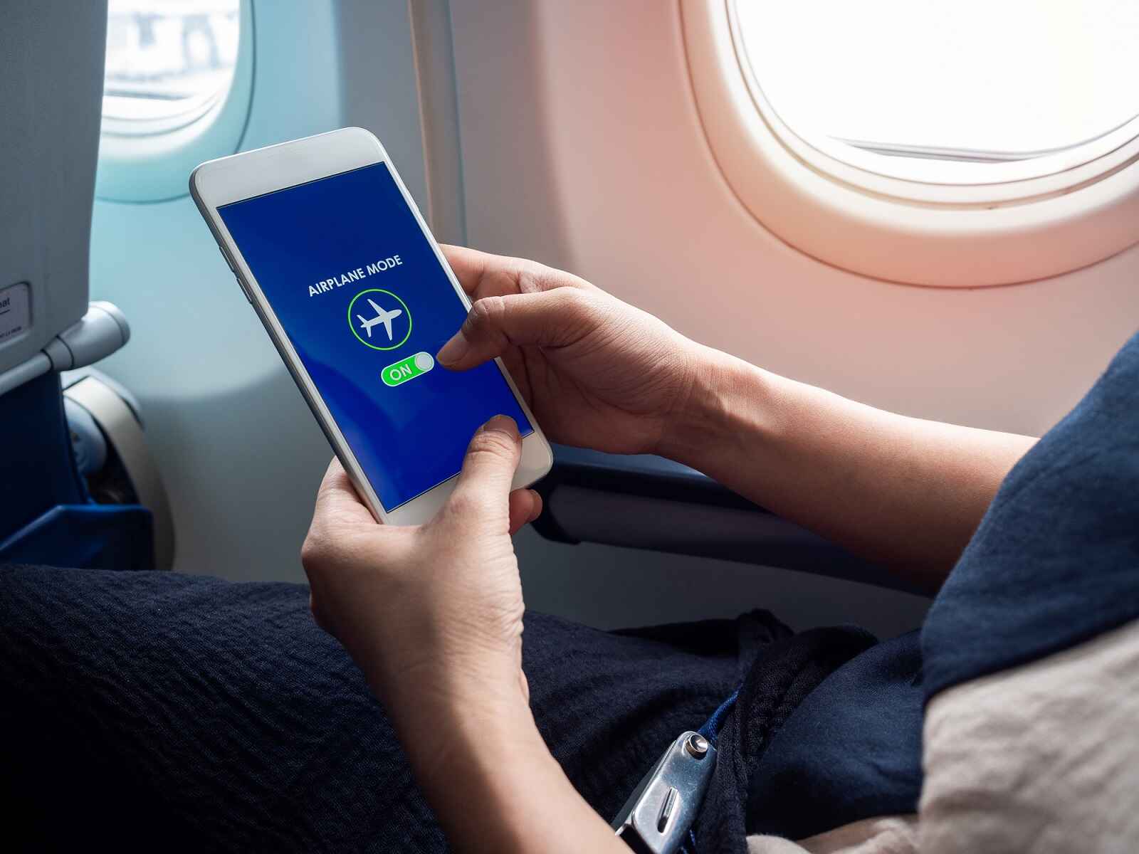 An airplane passenger putting a cell phone on airplane mode inside plane cabin