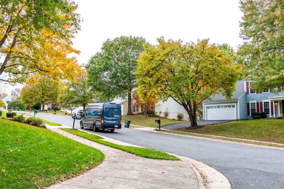 An amazon van driving down a residential street with fall colors