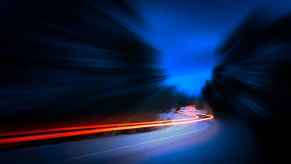 Brakes lights creating streaks of red across a dark frame road at night
