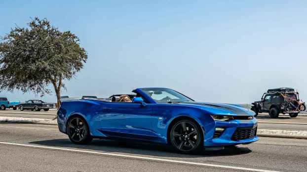 A blue convertible Camaro muscle car driving on a coastal road near the ocean