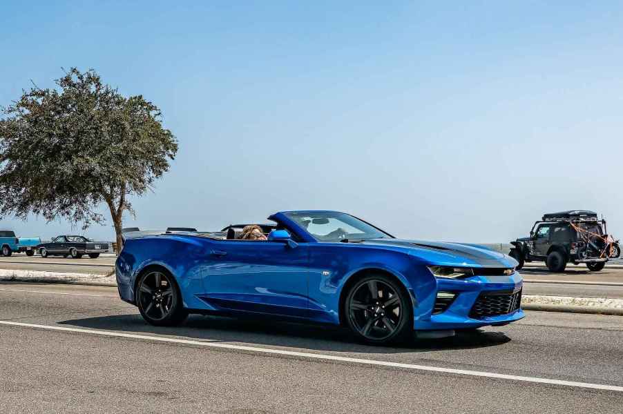 A blue convertible Camaro muscle car driving on a coastal road near the ocean