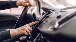 A woman touching her cell phone screen mounted to car interior dash while driving