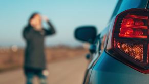A car broken down on the side of the road, and a woman looking distressed
