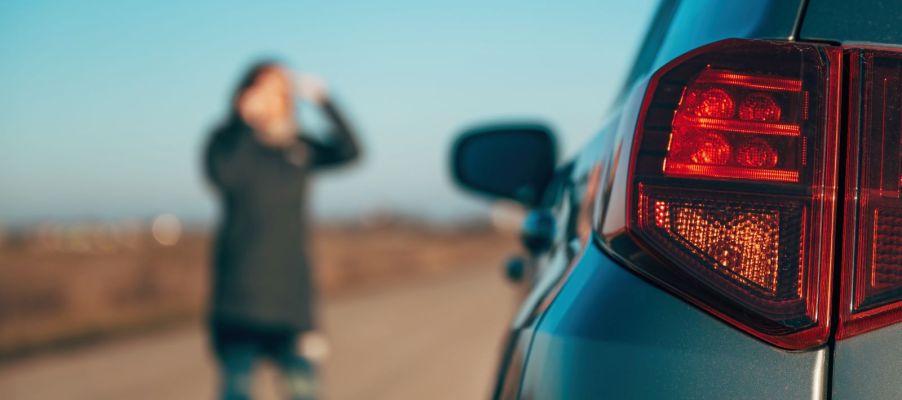 A car broken down on the side of the road, and a woman looking distressed