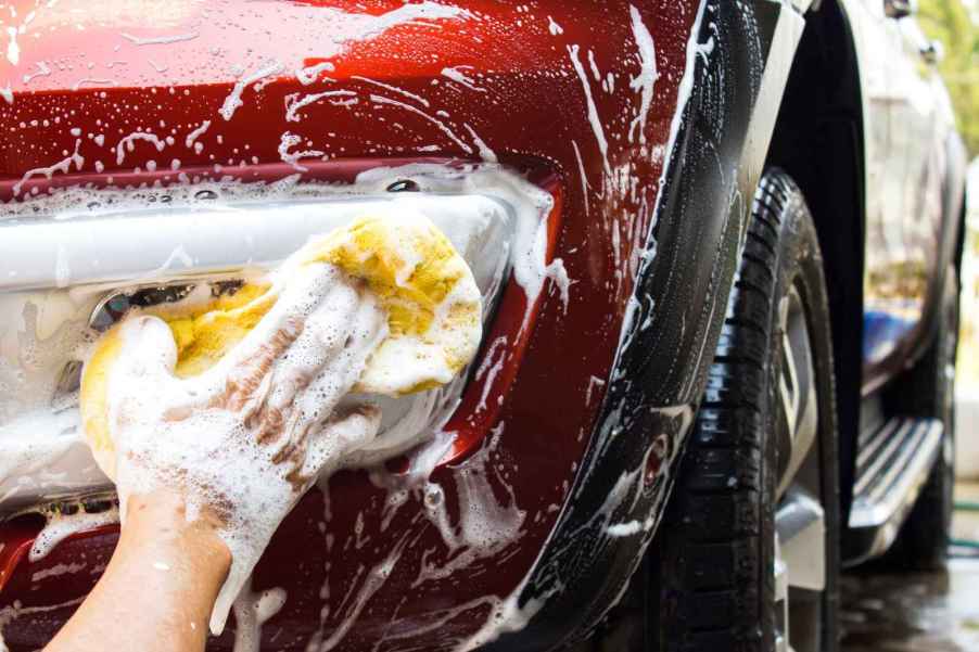 A man scrubbing the sudsy fog light of a red car during a car wash